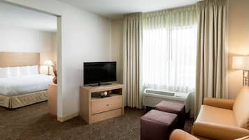 Une chambre d’hôtel avec un lit, une télévision, un canapé et une fenêtre avec des rideaux.