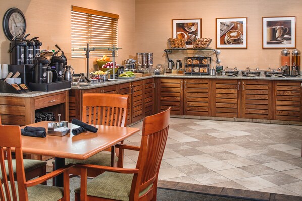 A kitchen with wooden cabinets, a dining table with chairs, and various kitchen appliances and utensils.
