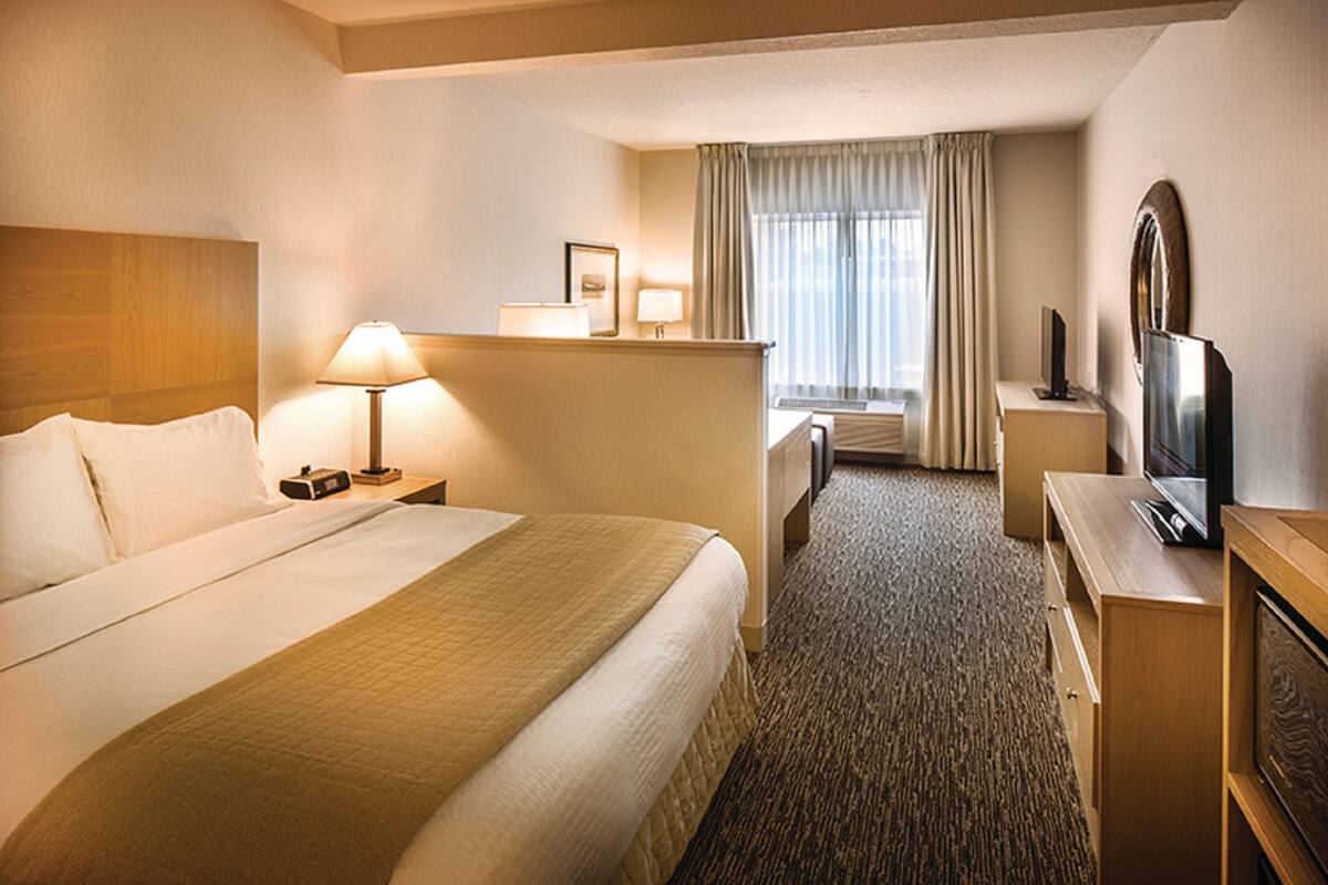 Habitación de hotel con una cama grande, un escritorio con lámpara, televisor y ventana con cortinas.