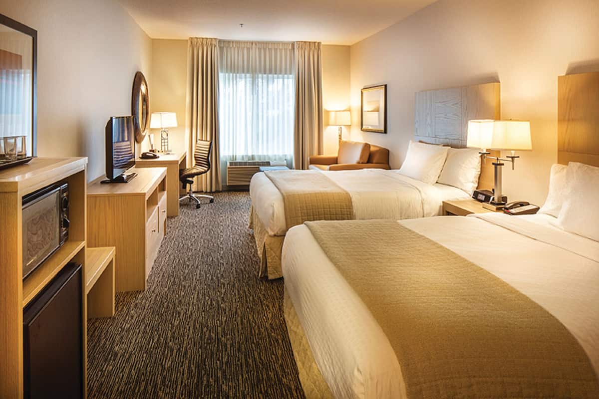 Habitación de hotel con dos camas, un escritorio, una computadora, una silla y un televisor.