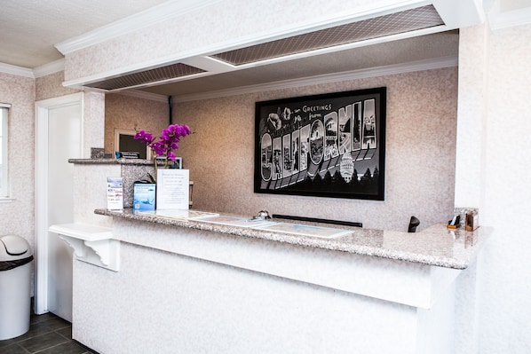 A reception area with a marble counter, a framed welcome sign, a trash bin, and a small plant.