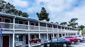 A motel with a two-story structure, a covered parking area, and a row of parked cars. - Pelican Inn Monterey (Monterey)