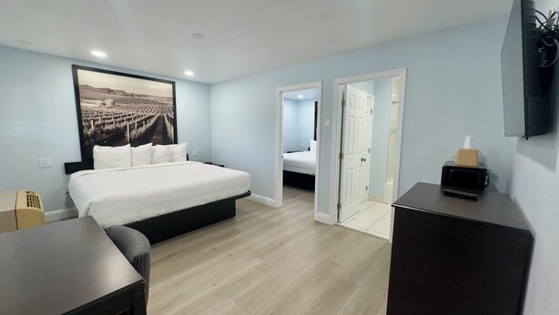 A hotel room with a bed, a desk, a chair, a television, and a door leading to another room. - Pelican Inn Monterey (Monterey)