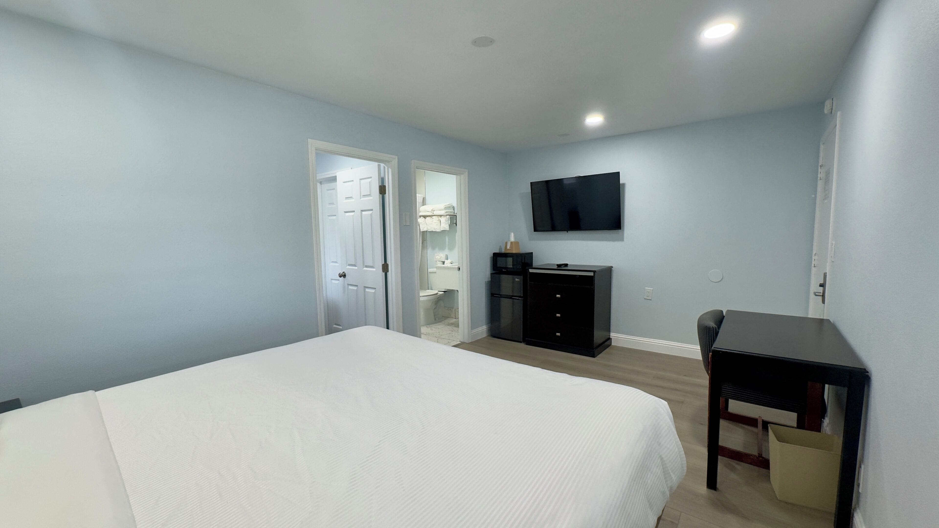 Une chambre à coucher comprenant un lit, une commode, un téléviseur et une porte donnant sur une salle de bain.