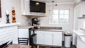 A compact kitchen with white cabinets, a microwave, a coffee machine, and a TV mounted above the counter. - Pelican Inn Monterey (Monterey)