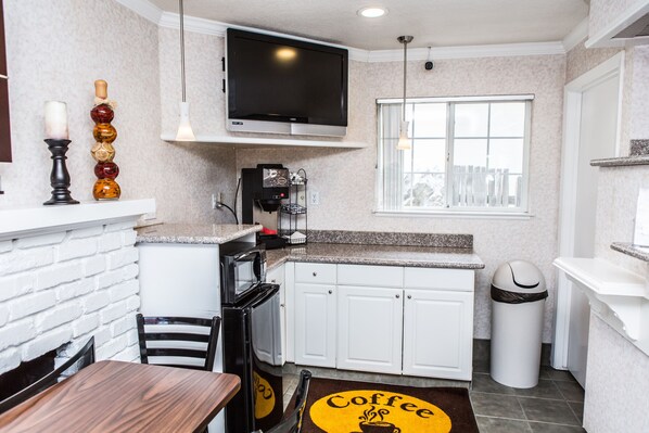 A compact kitchen with white cabinets, a microwave, a coffee machine, and a TV mounted above the counter.