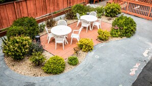A patio with a wooden fence, white plastic chairs, and small potted plants. - Pelican Inn Monterey (Monterey)