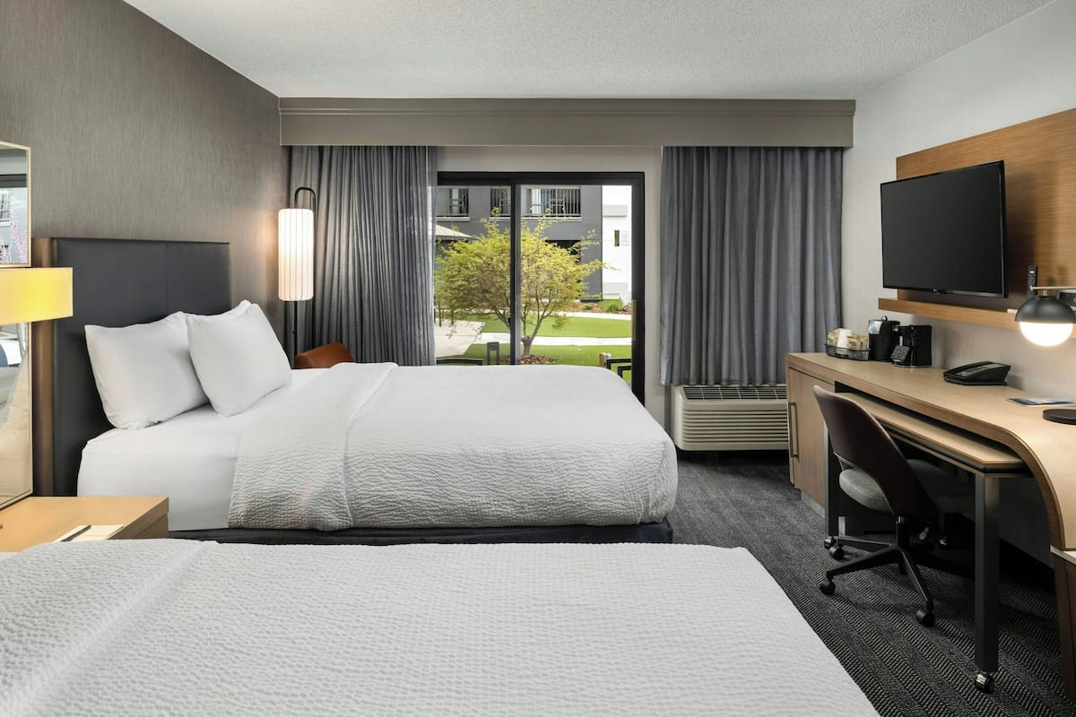 Een hotelkamer met een groot bed, een bureau, een stoel, een televisie en een raam met gordijnen.