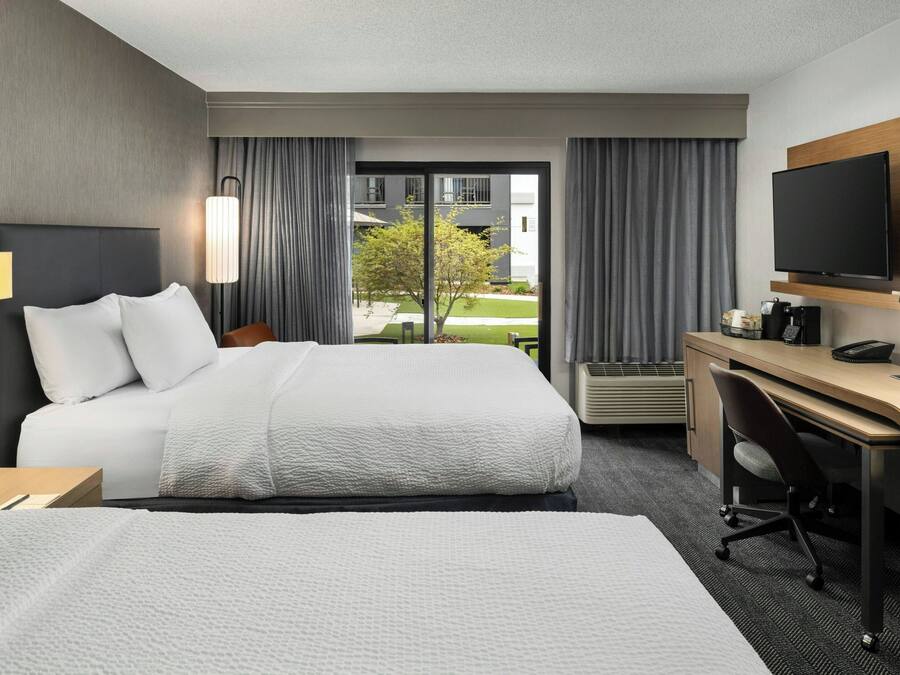A hotel room with a large bed, a desk, a chair, a TV, and a window with curtains.