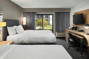 Une chambre d’hôtel avec un grand lit, un bureau, une chaise, une télévision et une fenêtre avec des rideaux.