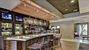 Un espace bar moderne doté d’un long comptoir, de nombreux tabourets et d’une grande variété de bouteilles et de verres.