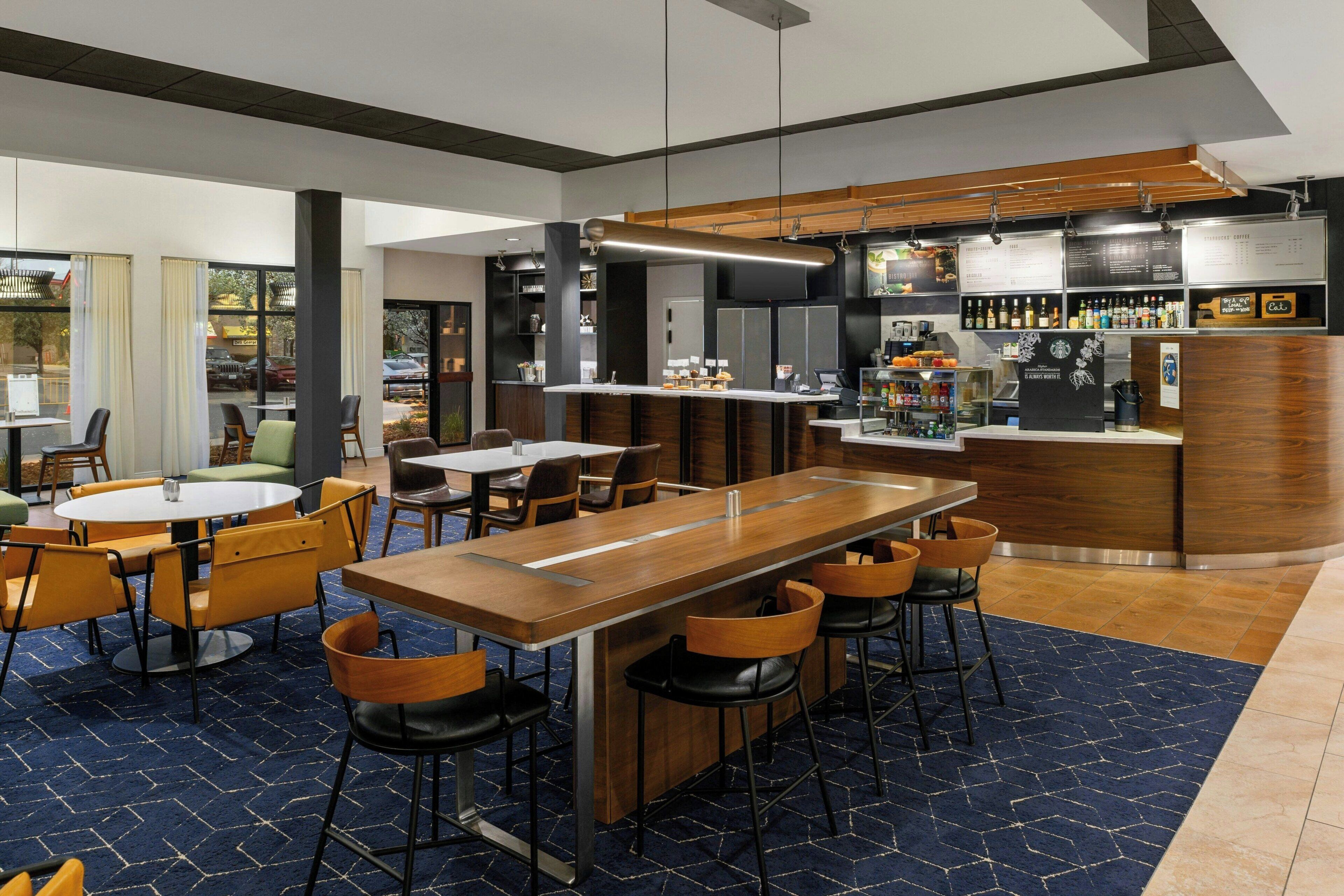 A modern bar area with a long counter, multiple stools, and a menu board.
