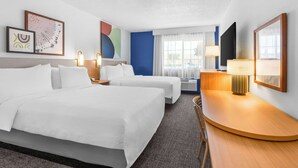 A hotel room with two beds, a desk, a chair, a TV, and artwork on the walls.
