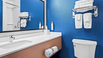 A bathroom with a blue wall, white sink, and toilet. There are towels and toiletries on the counter.