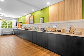 A modern kitchen with a long counter, various food items, and a green accent wall.