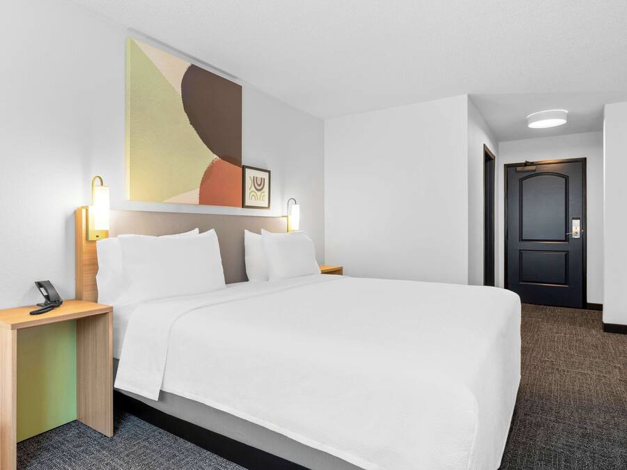 Quarto de hotel com cama, mesas de cabeceira, escrivaninha e porta.