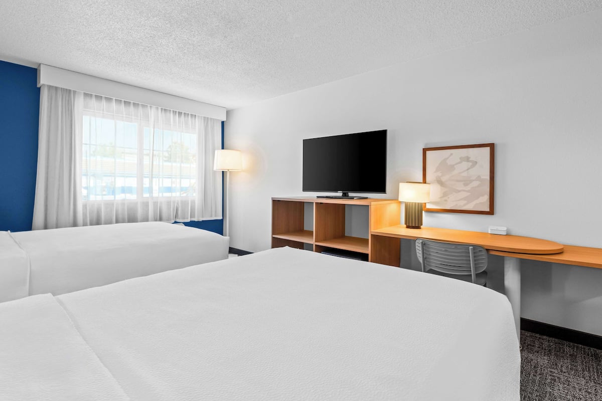 A hotel room with two beds, a TV, a desk with a lamp, and a window with curtains.