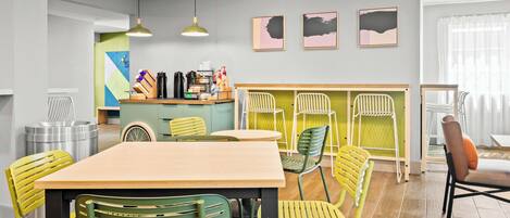A dining area with a wooden table and green chairs, a kitchen area with a counter and various appliances, and a seating area with a couch and chairs.