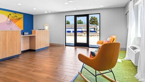 A reception area with a wooden reception desk, a colorful abstract painting, a large window with a view of a building, and a green carpeted area with a chair.