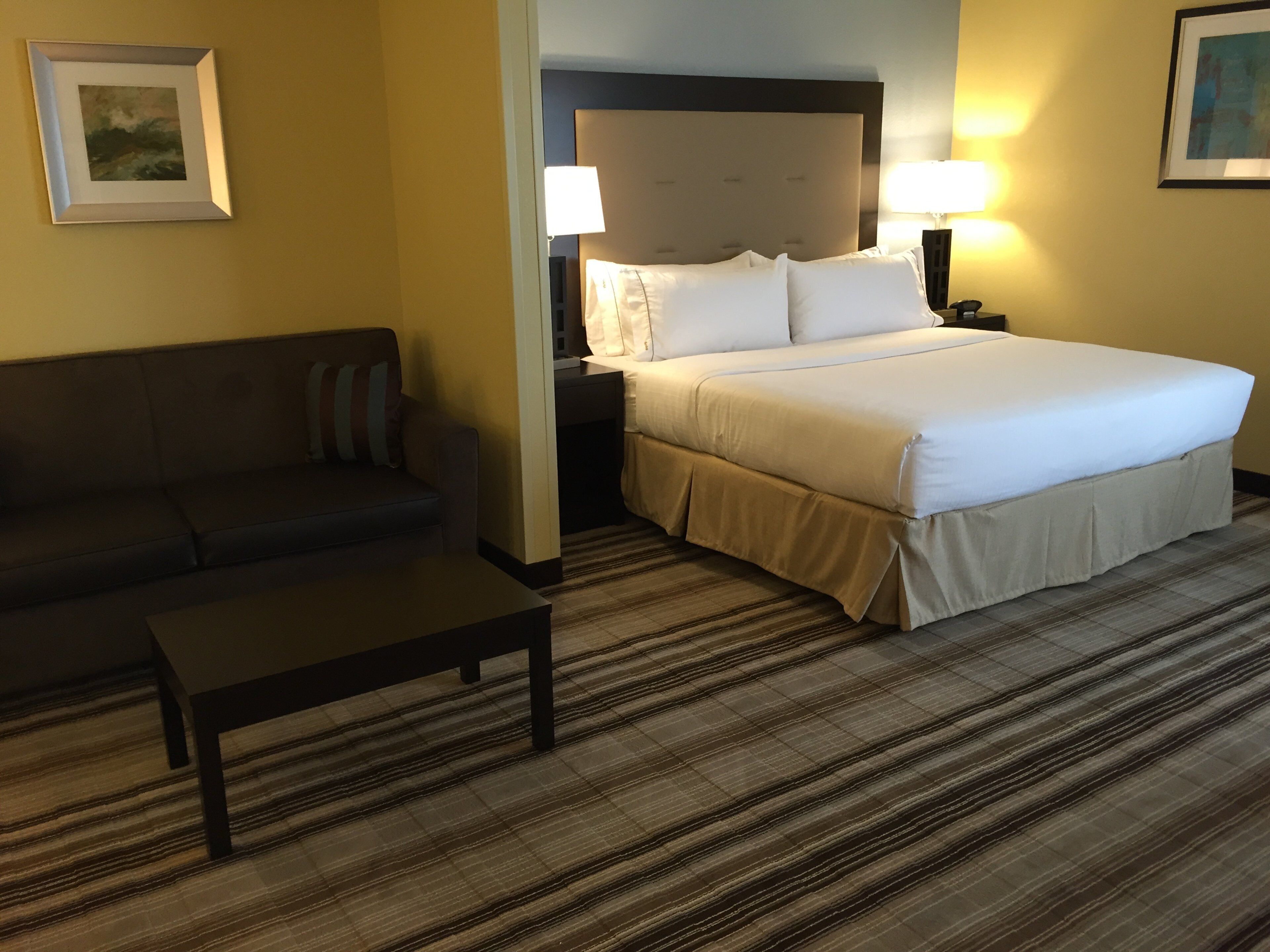Una habitación de hotel con cama, sofá, mesita de noche y lámpara.