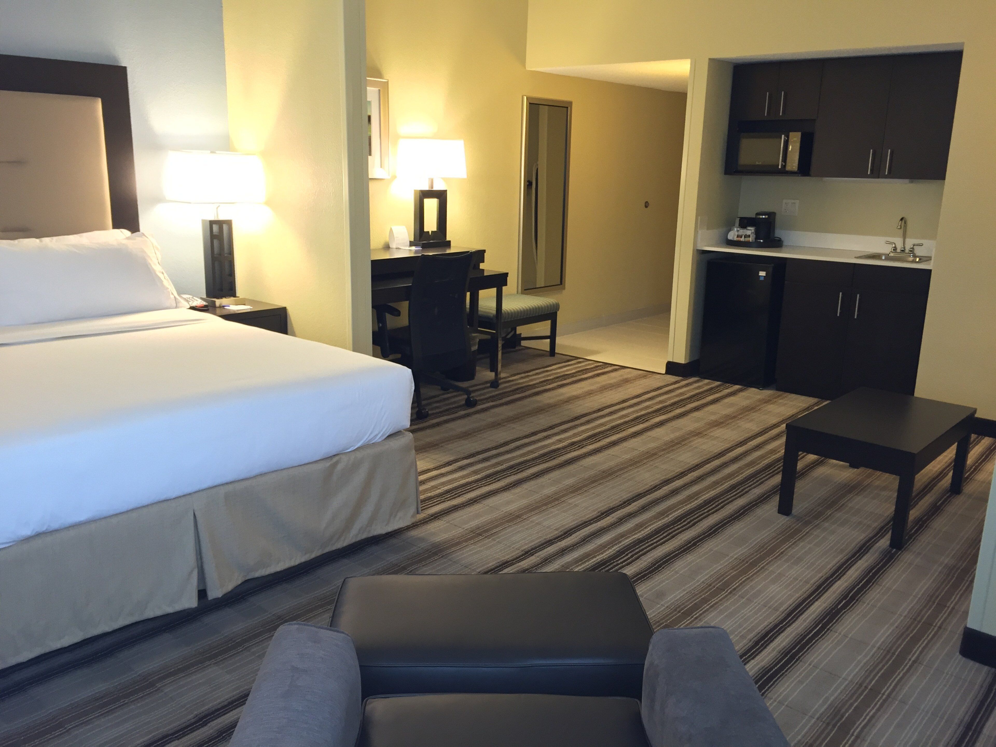 Una habitación de hotel con cama, escritorio, silla, kitchenette y una pequeña mesa.
