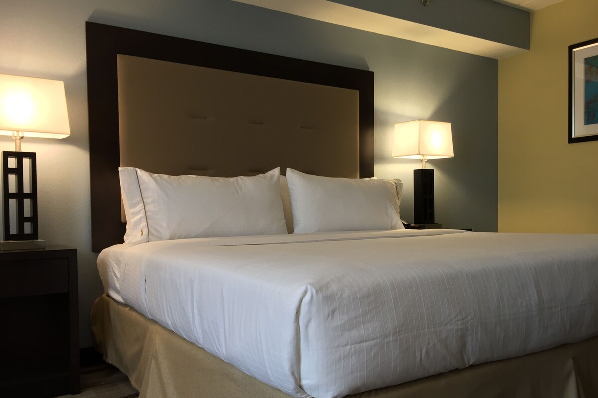 A neatly made bed with white linens, a dark headboard, and two bedside lamps on either side.