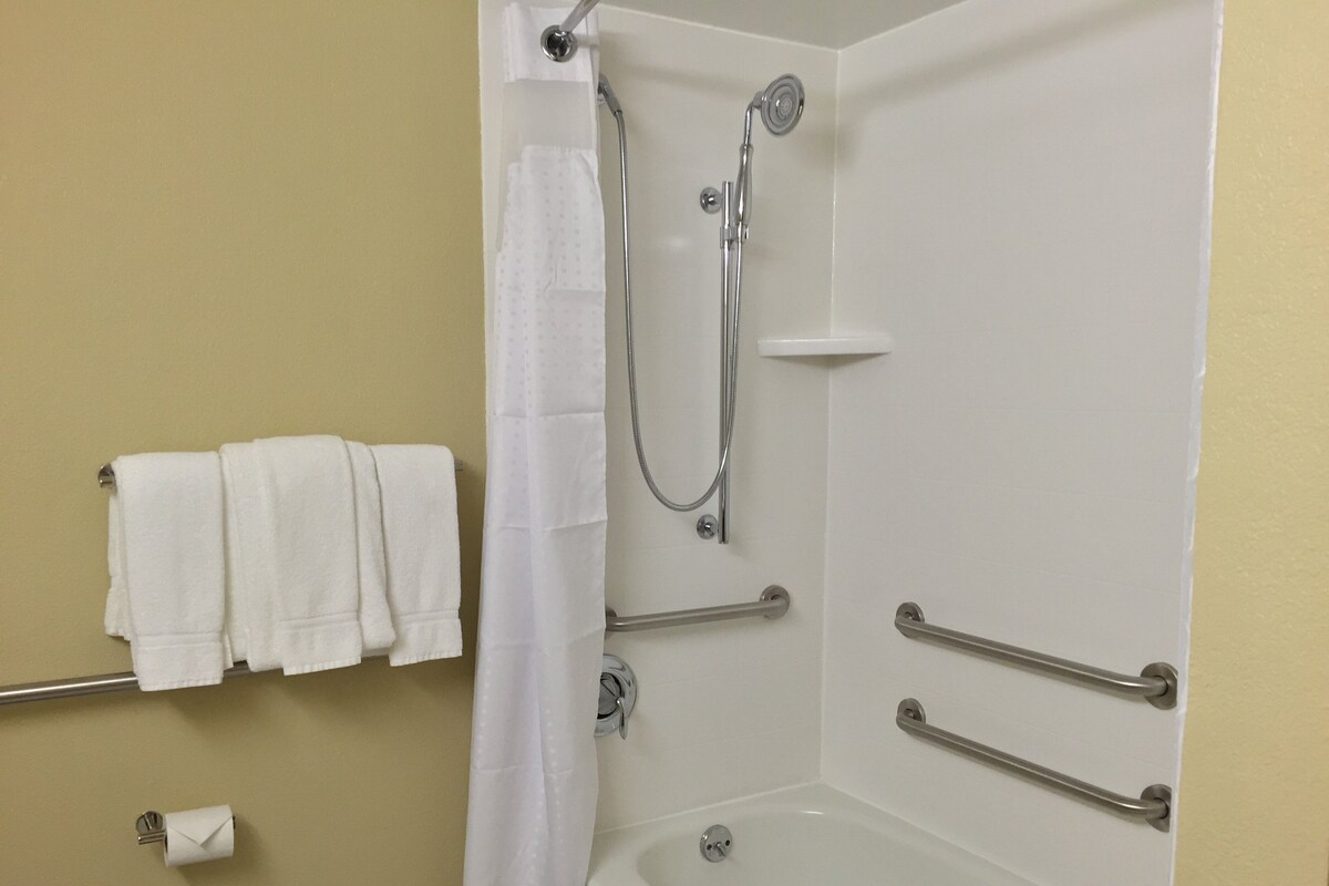 A bathroom with a shower, a bathtub, and handrails.