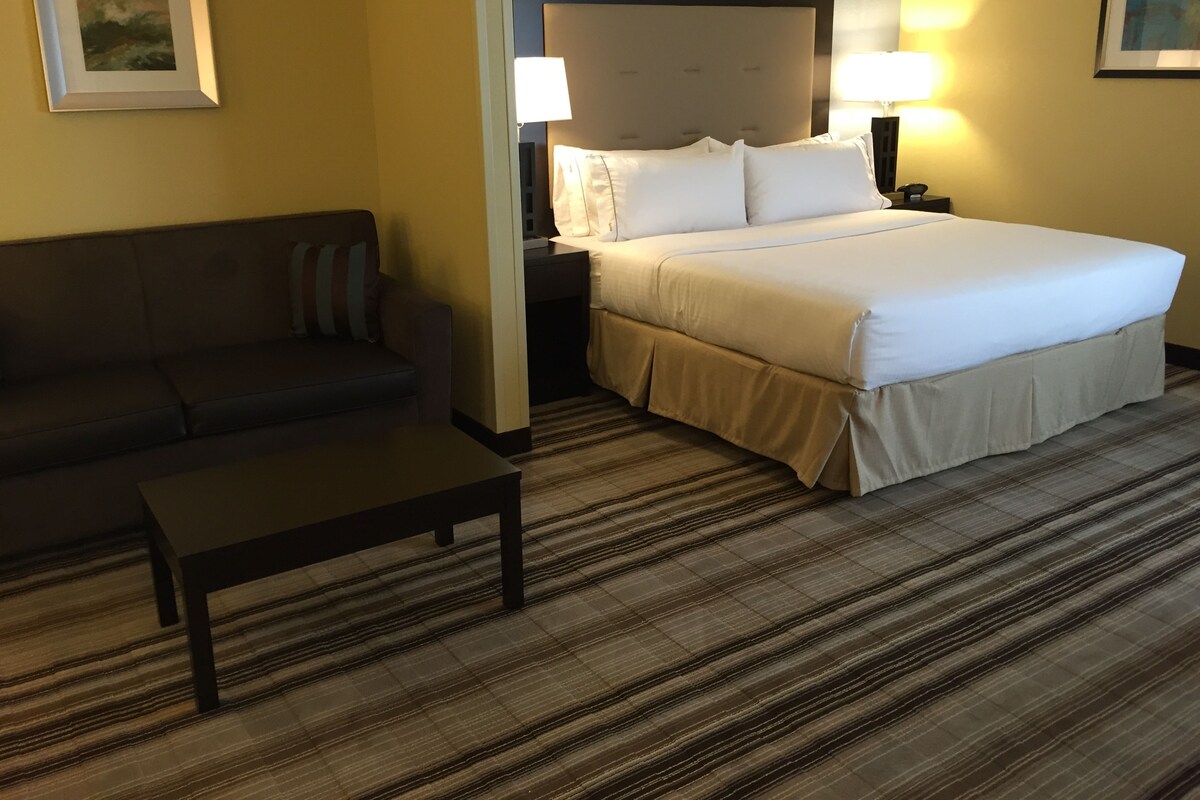 A hotel room with a bed, a sofa, a nightstand, and a lamp.