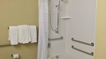 A bathroom with a shower, grab bars, a towel rack, and a toilet paper holder.