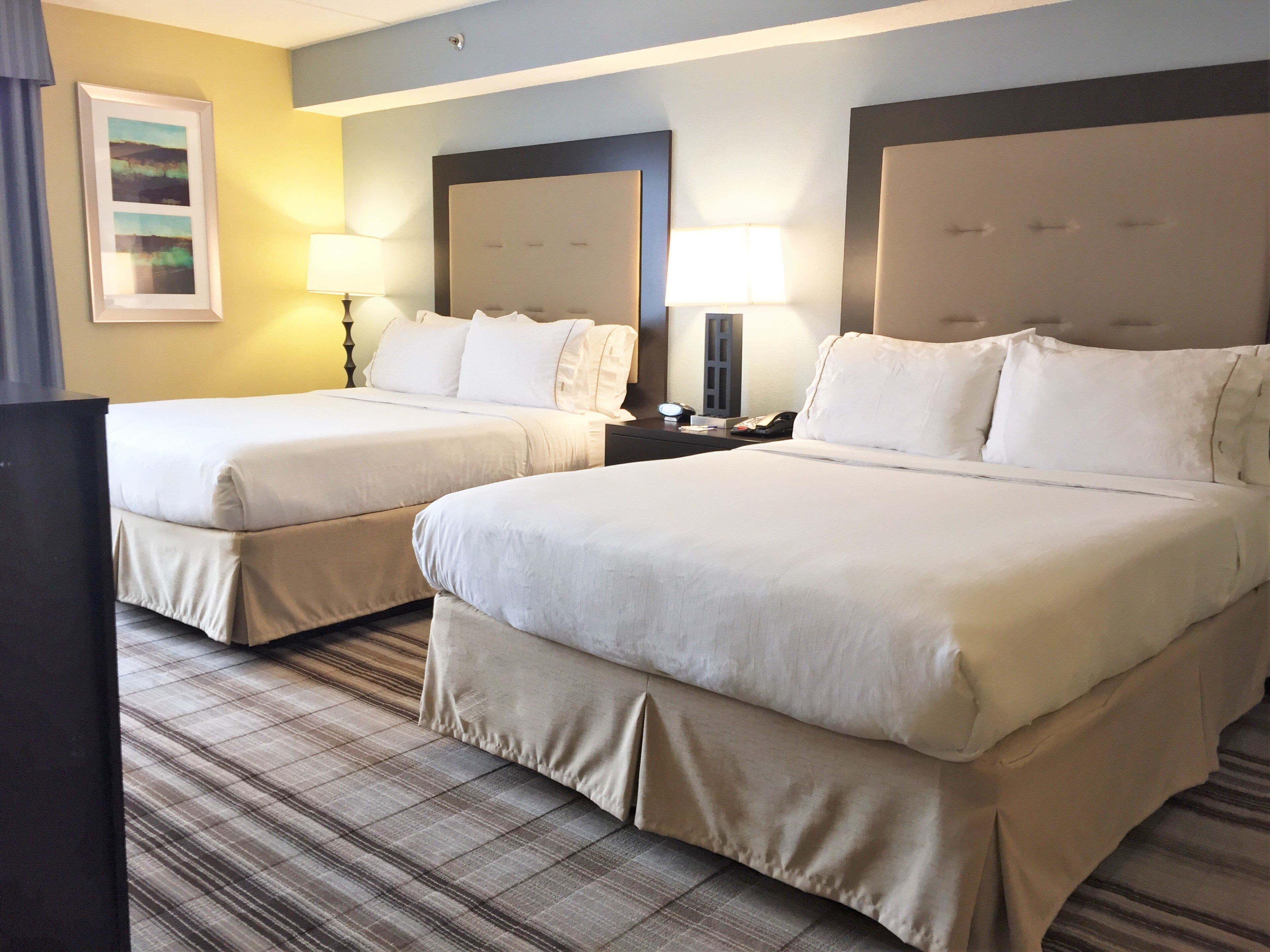 A hotel room with two beds, a flat-screen TV, a nightstand with a lamp, and a painting on the wall.