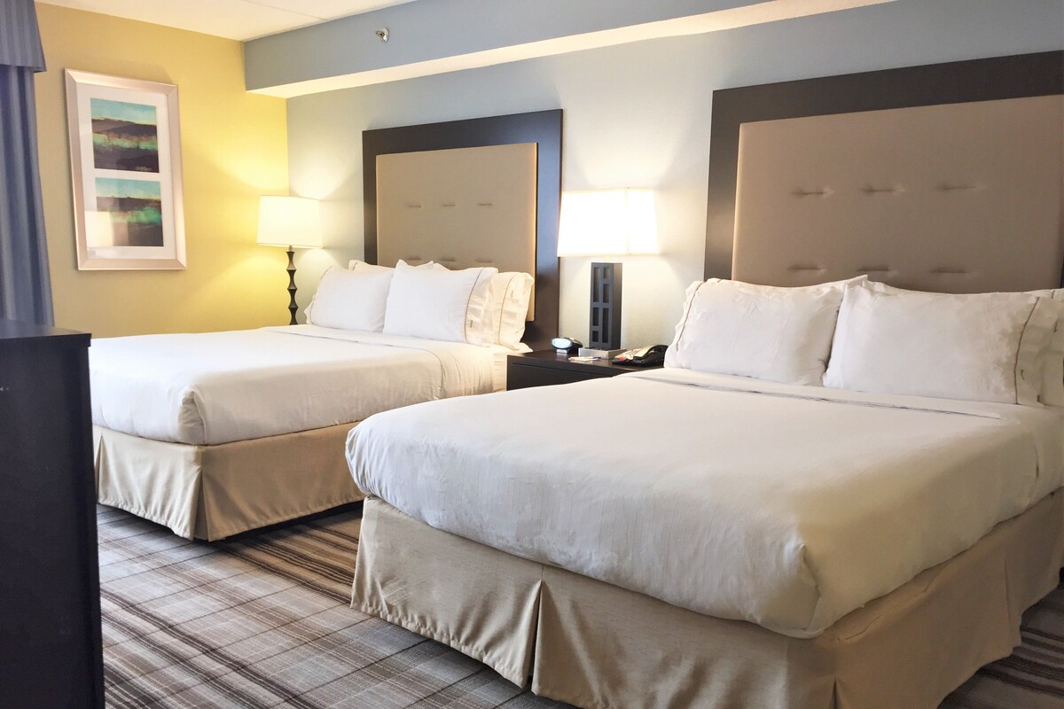 A hotel room with two beds, a flat-screen TV, a nightstand with a lamp, and a painting on the wall.
