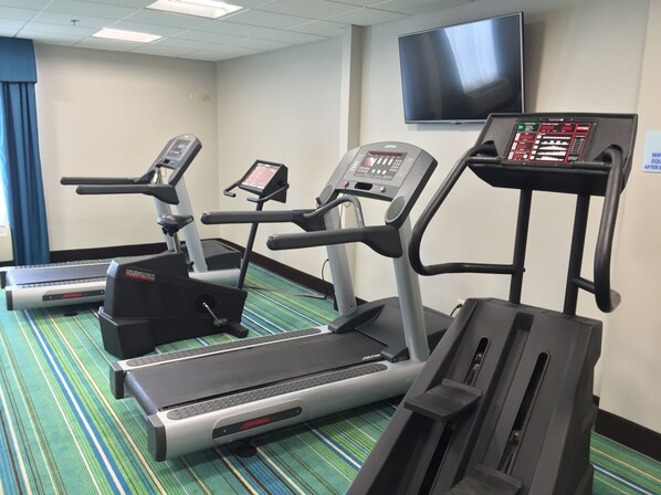 Un gimnasio con cintas de correr, una bicicleta estática y un televisor montado en la pared.