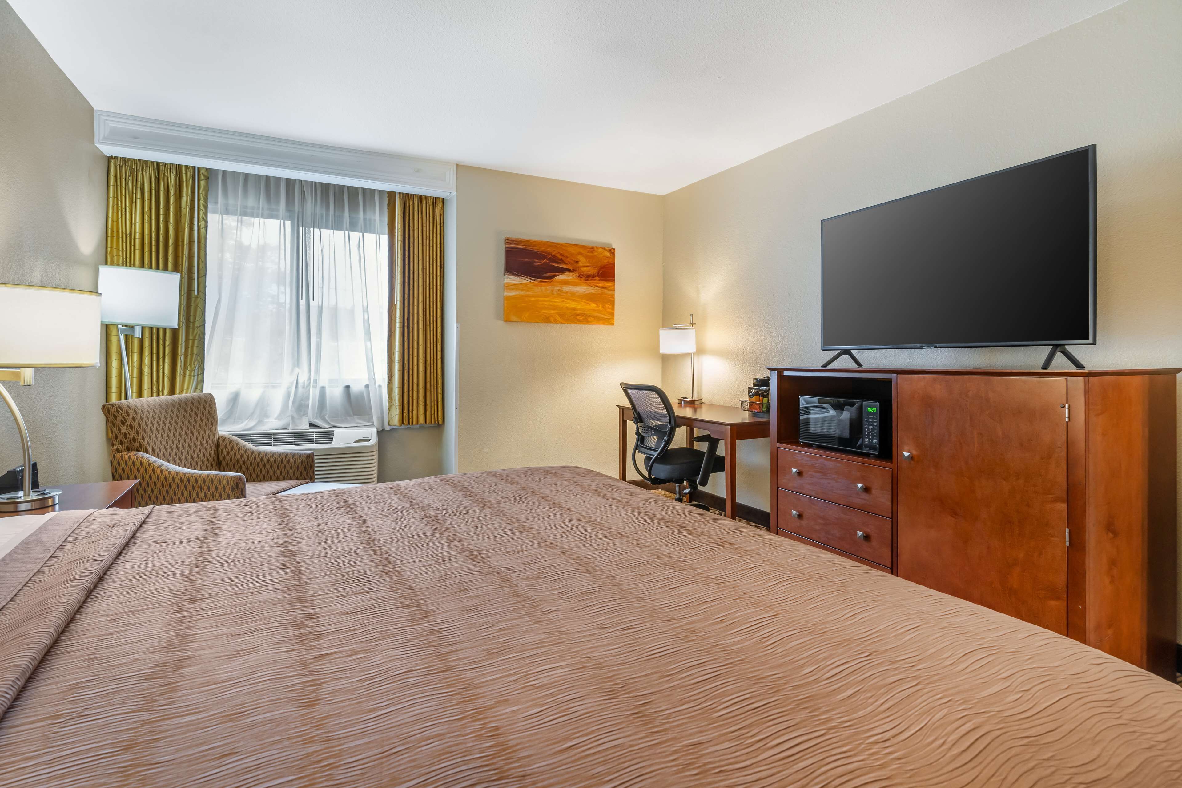 Une chambre d’hôtel avec un grand lit, un bureau avec un ordinateur, une télévision et une chaise.
