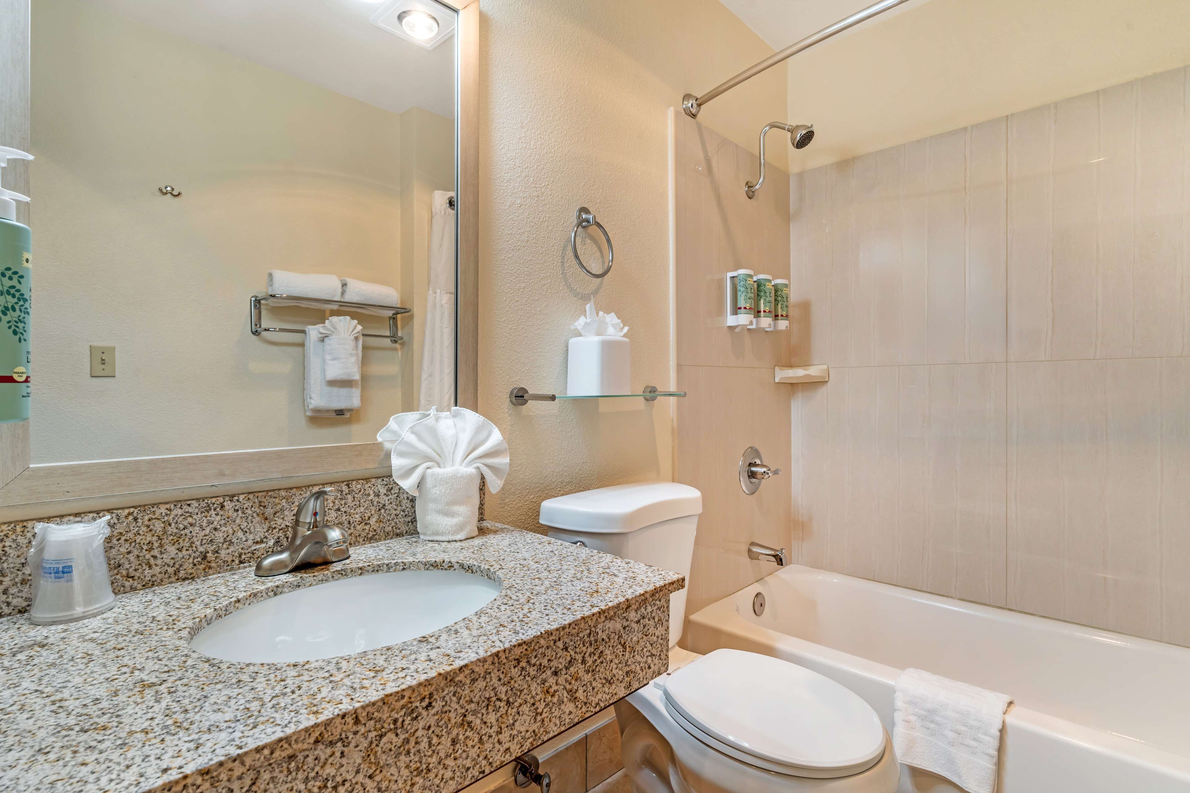 A bathroom with a granite countertop sink, a toilet, a bathtub, and a glass shower enclosure.