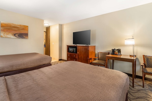 Habitación de hotel con dos camas, un televisor, un escritorio con lámpara y una silla.