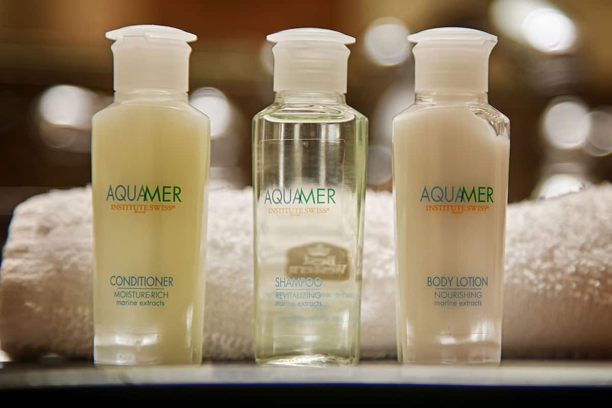 Three bottles of Aquamer products: conditioner, shampoo, and body lotion, with a towel in the background.