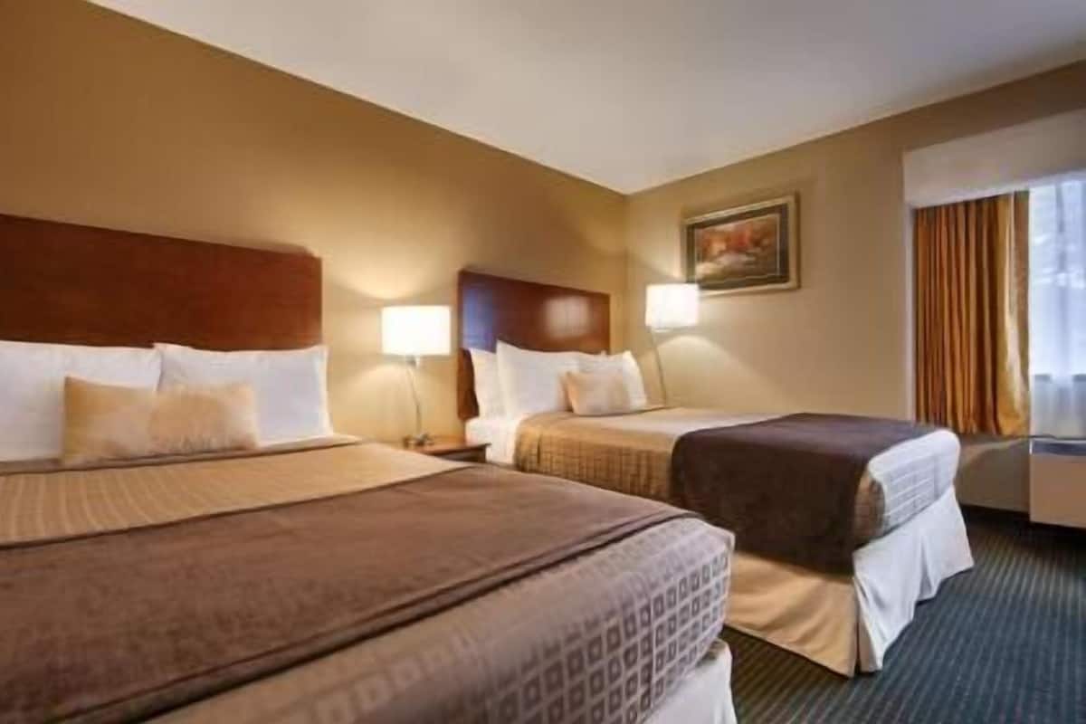 A hotel room with two beds, a painting on the wall, and a window with curtains.