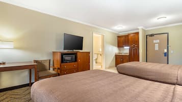 A hotel room with two beds, a desk with a chair, a television, and wooden cabinets.