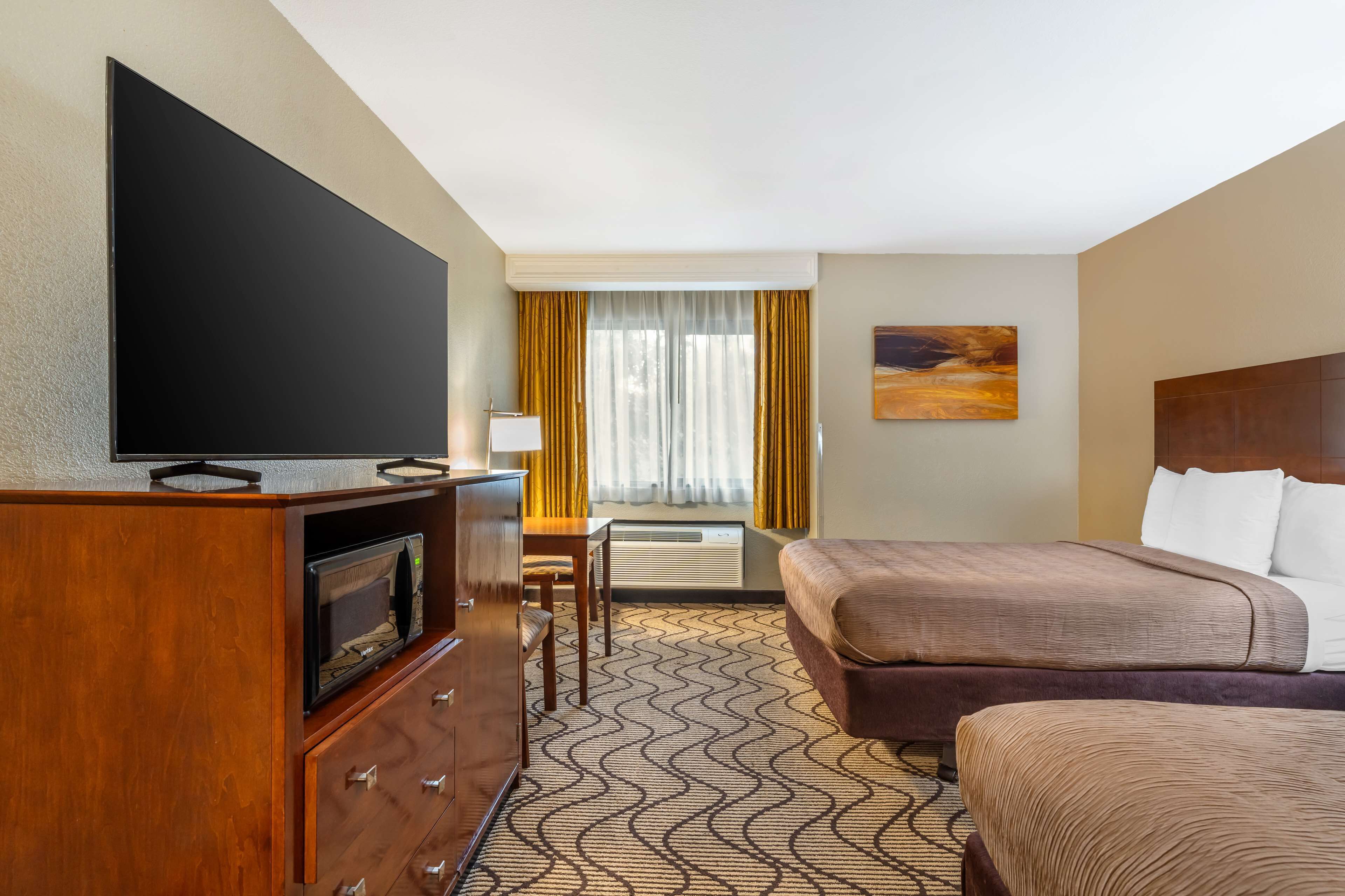 A hotel room with a bed, a TV, a desk, and a window with curtains.