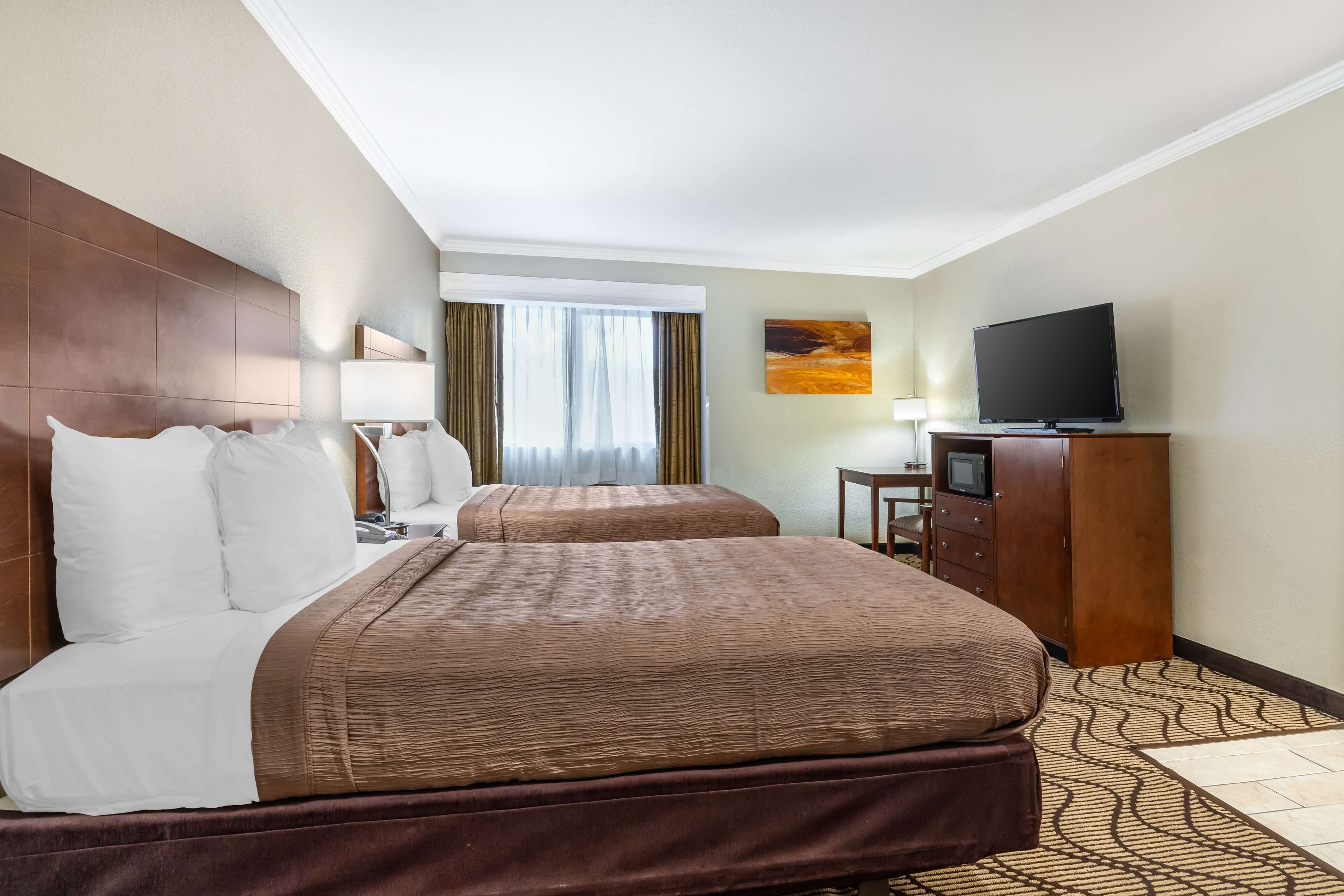 A hotel room with two beds, a TV, a desk, and a window with curtains.