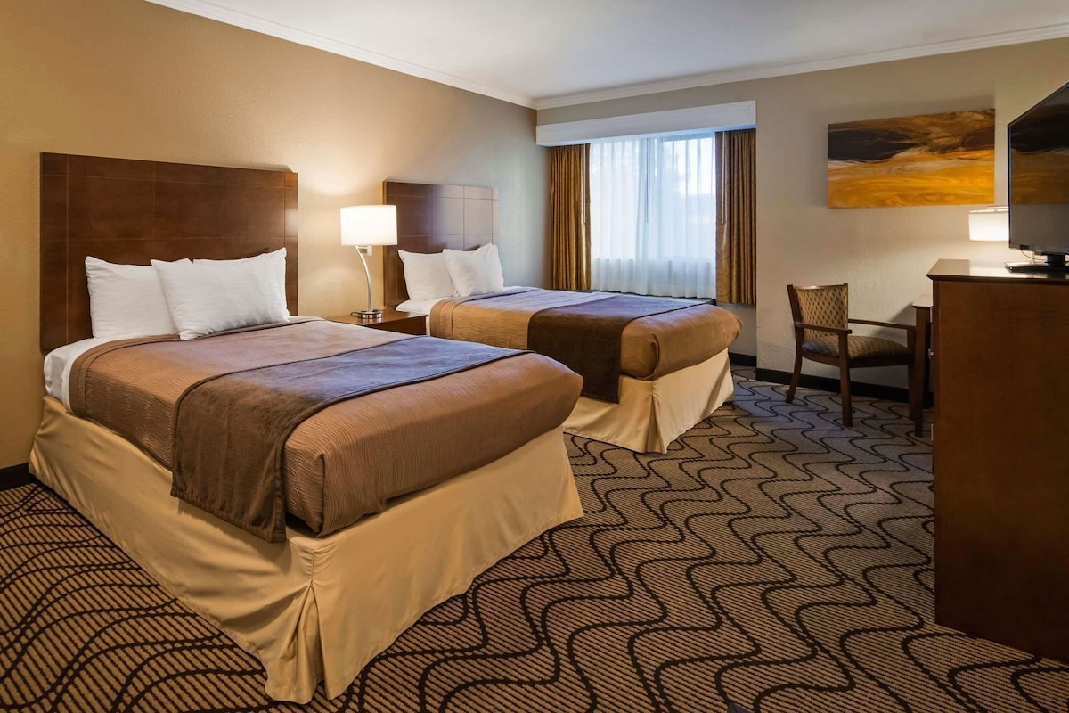 A hotel room with two beds, a desk, a chair, and artwork on the walls.