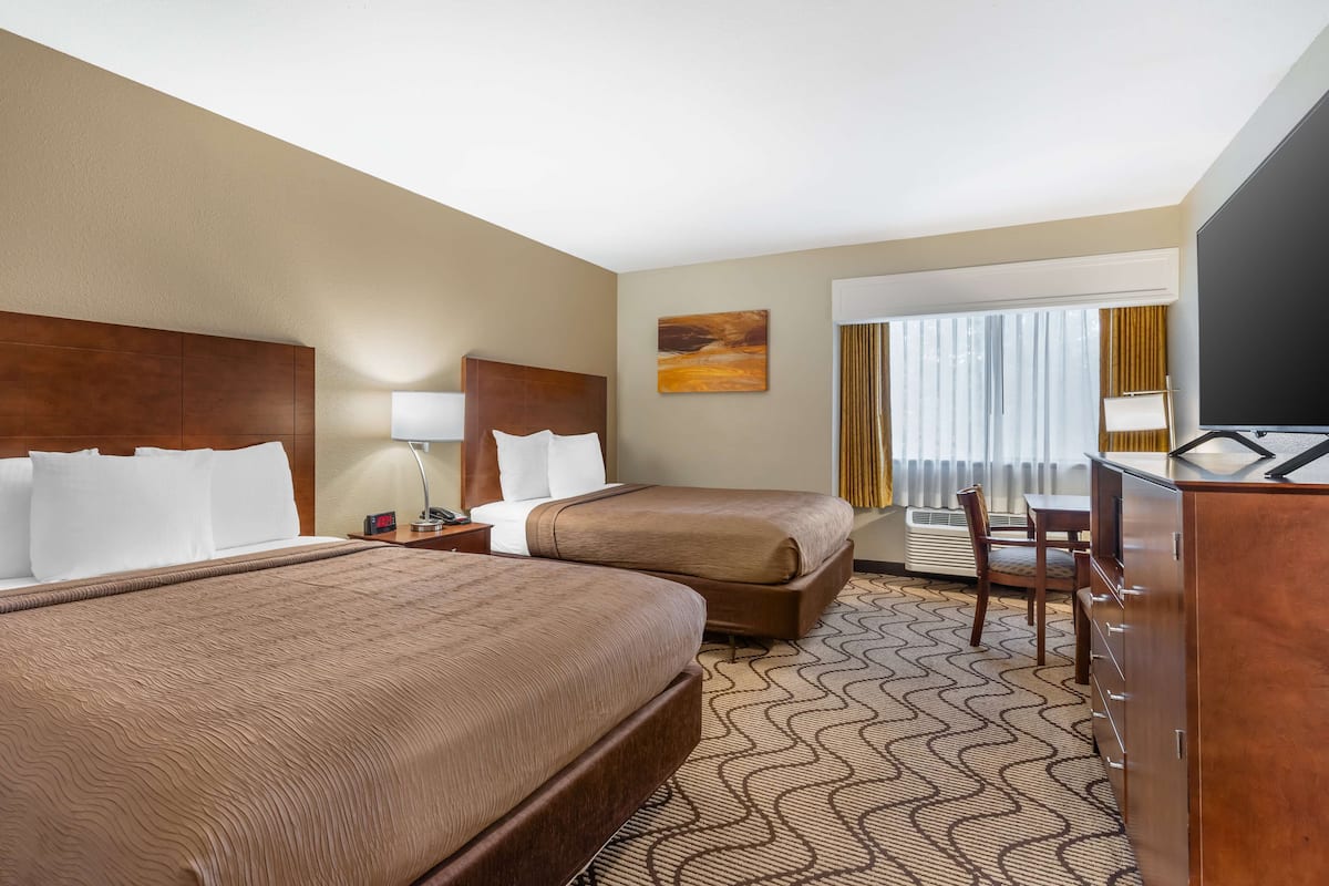 A hotel room with two beds, a desk, a chair, a TV, and a window with curtains.