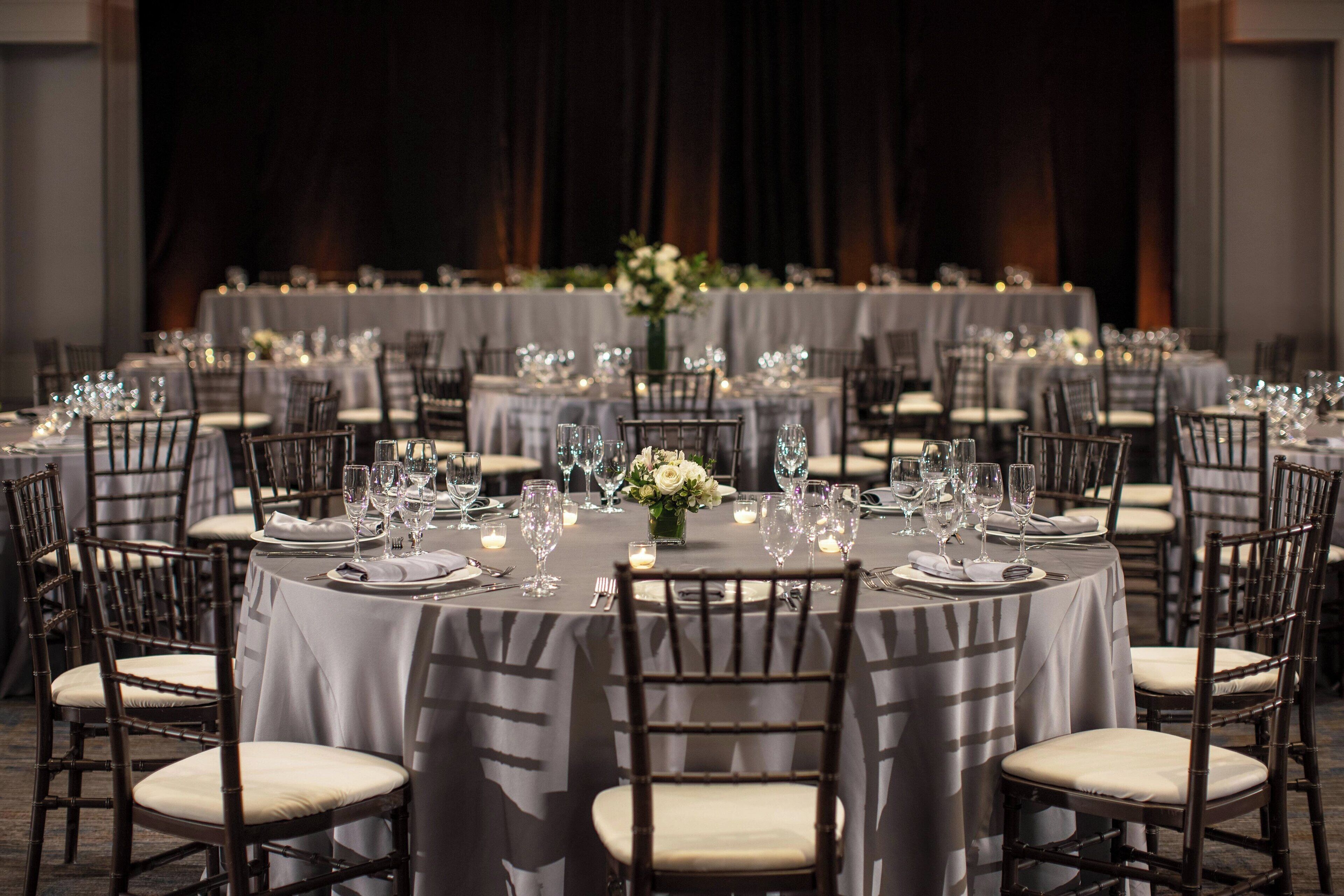 A formal dining room with round tables, chairs, and a central floral arrangement.