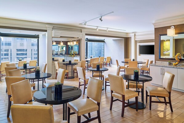 A spacious dining area with multiple tables and chairs, a kitchen area with modern appliances, and large windows offering views of the city. - The Westin Chicago River North (Chicago)