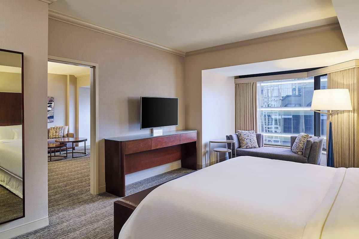 Une chambre d’hôtel dotée d’un grand lit, d’un téléviseur posé sur une console en bois, d’un coin salon avec un canapé et des fauteuils, et d’une fenêtre avec des rideaux.