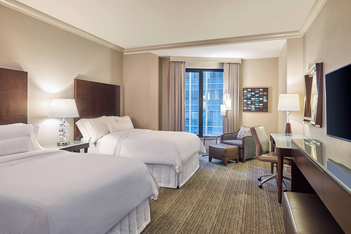 Une chambre d’hôtel avec deux lits, un bureau, une chaise, une télévision et une fenêtre avec des rideaux.