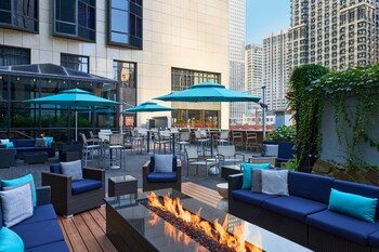 Relax in style with sofas and chairs arranged around a central fire feature, shaded by umbrellas in a vibrant urban setting. at The Westin Chicago River North