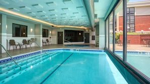 En swimmingpool med kristallklart blått vatten, en kakelbeklädd terrass och en glasvägg som ger utsikt över omgivningen.