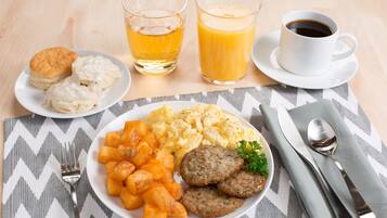 A breakfast plate with biscuits, scrambled eggs, hash browns, and sausage links, accompanied by two glasses of orange juice and a cup of coffee.
