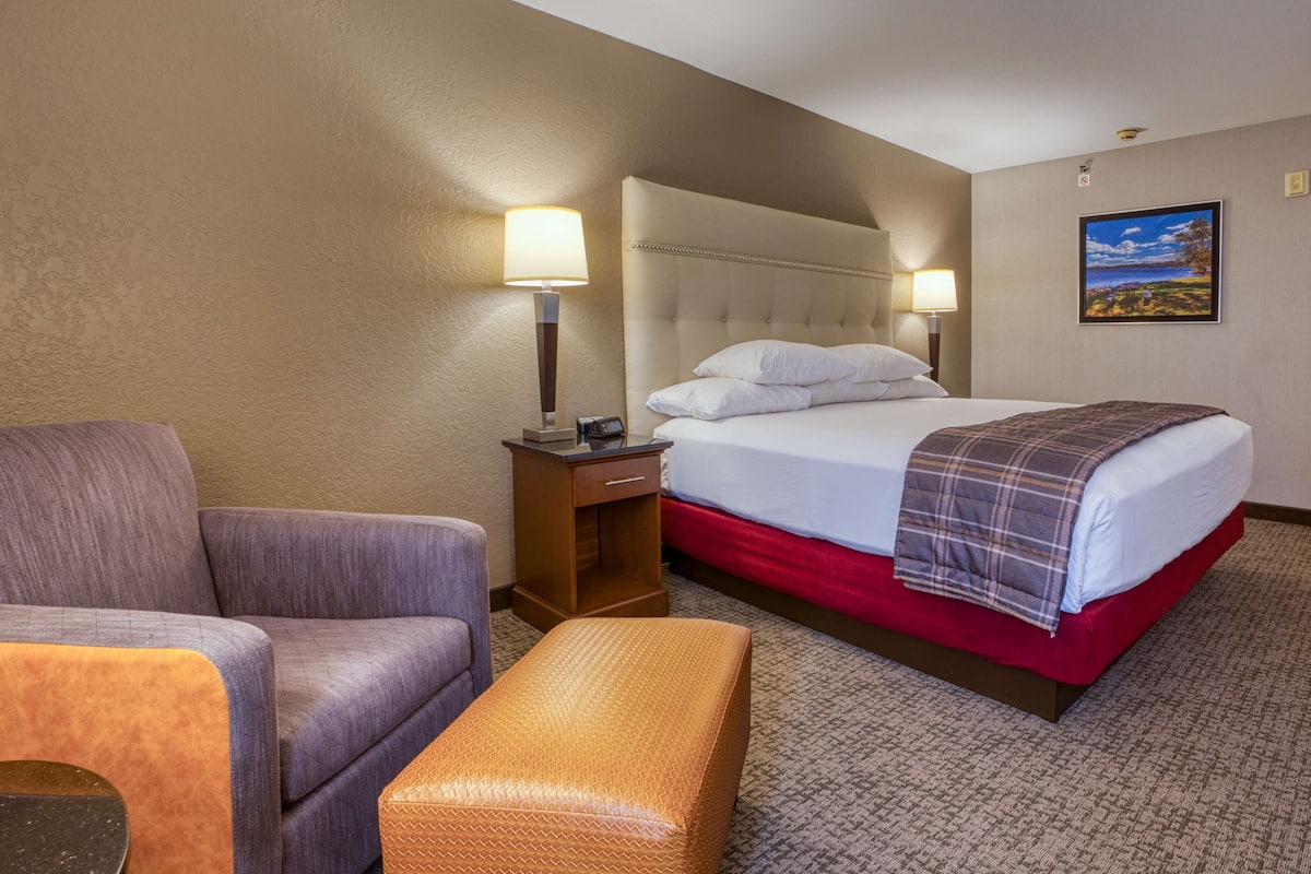 A hotel room with a bed, a chair, a nightstand, and a lamp.